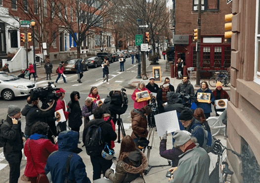crowd standing on the sidewalk holding signs